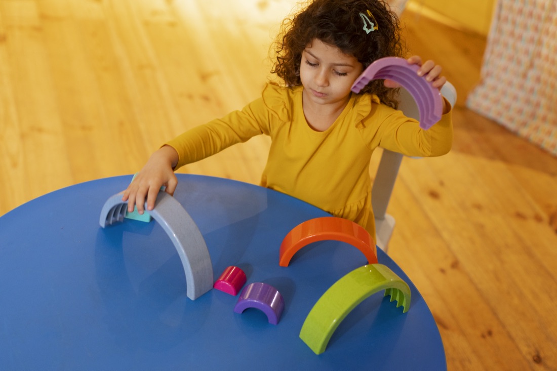 Kind speelt met houten regenboogbogen aan tafel